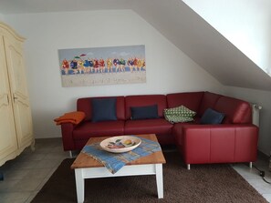 A red leather sofa with multiple cushions, a wooden coffee table with a bowl and placemat, and a painting above the sofa.