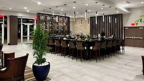 A modern bar area with a central island, multiple seating options, and a large potted plant. - SUITE 167m2, facing the beach, sleeps 8, DBC, sharing JW Marriot facilities. (Oyster pond)
