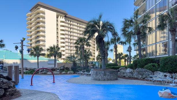 A hotel with a swimming pool, palm trees, and a large building in the background. - Tipsy Turtle Edgewater Villa 2901-Pickleball, Tennis, Fitness Center Included! 1st Floor-End Unit (Panama City Beach)