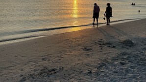 Escena de playa con dos personas caminando por la orilla al atardecer.