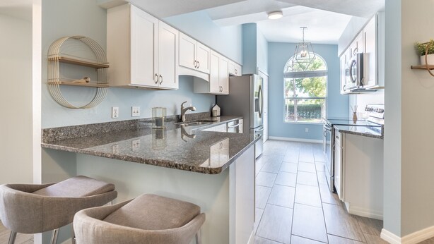 Una cocina moderna con armarios blancos, encimeras de granito y una isla central con taburetes de bar.