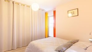 A bedroom with a bed, curtains, a bedside table, and a wall-mounted light fixture. - Résidence Le Centre by Interhome (Meschers)