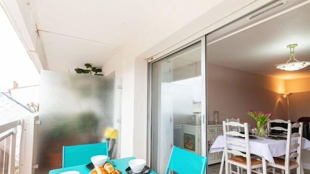 A dining area with a turquoise table set for four, white chairs, and a view of the kitchen through a glass door. - Résidence Le Centre by Interhome (Meschers)