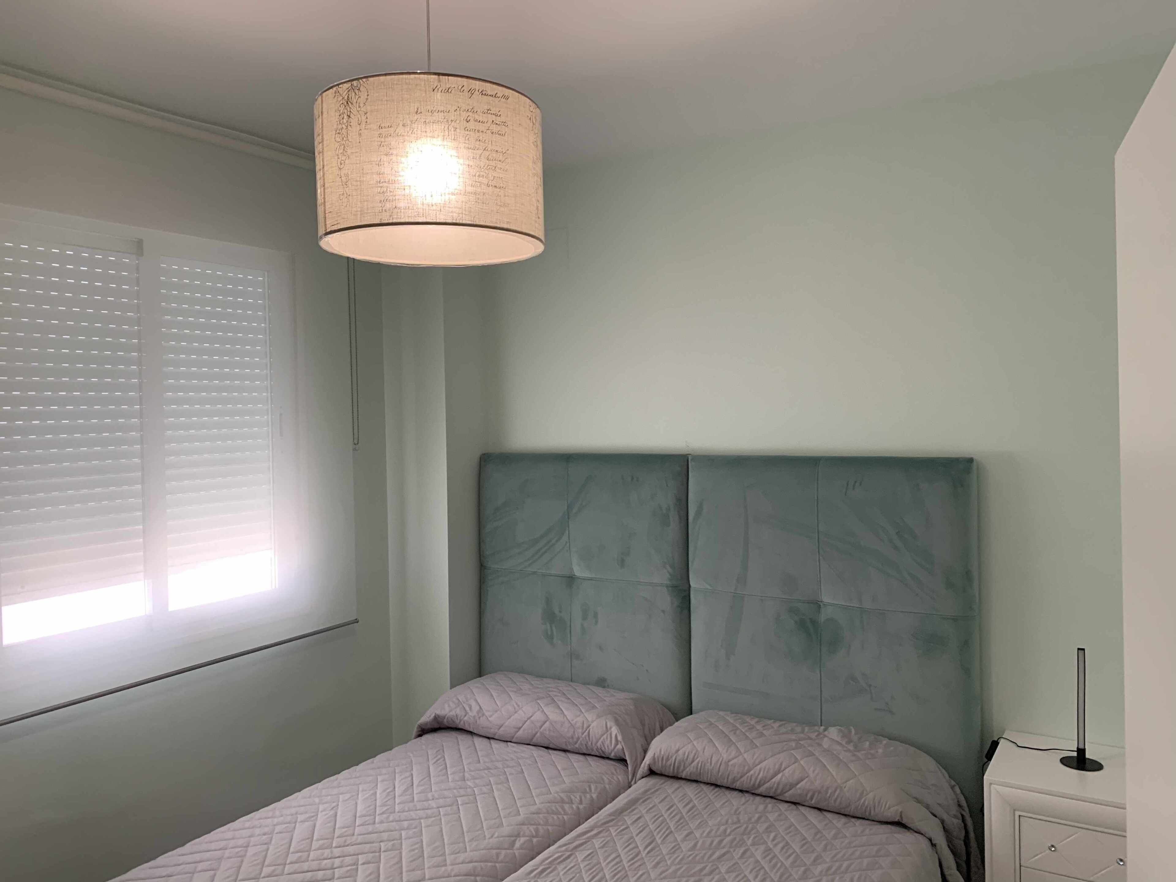 Un dormitorio con cama, mesita de noche y lámpara colgante.