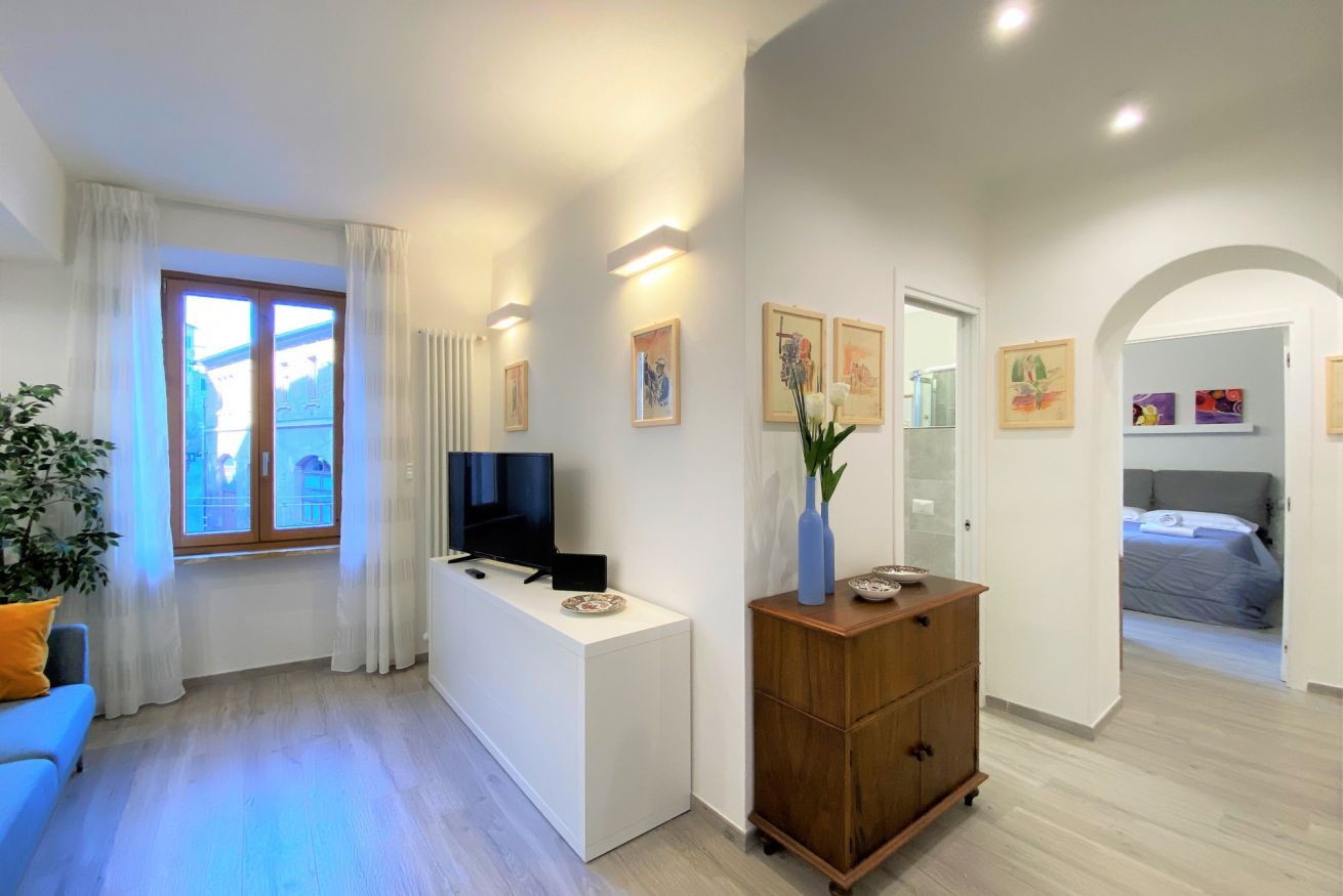 A modern living room with a TV, a wooden cabinet, and a sofa. There is a window with curtains and a view of a balcony.