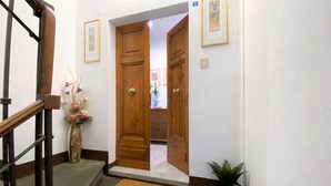 Un pasillo con puertas de madera, una escalera y un florero con flores.