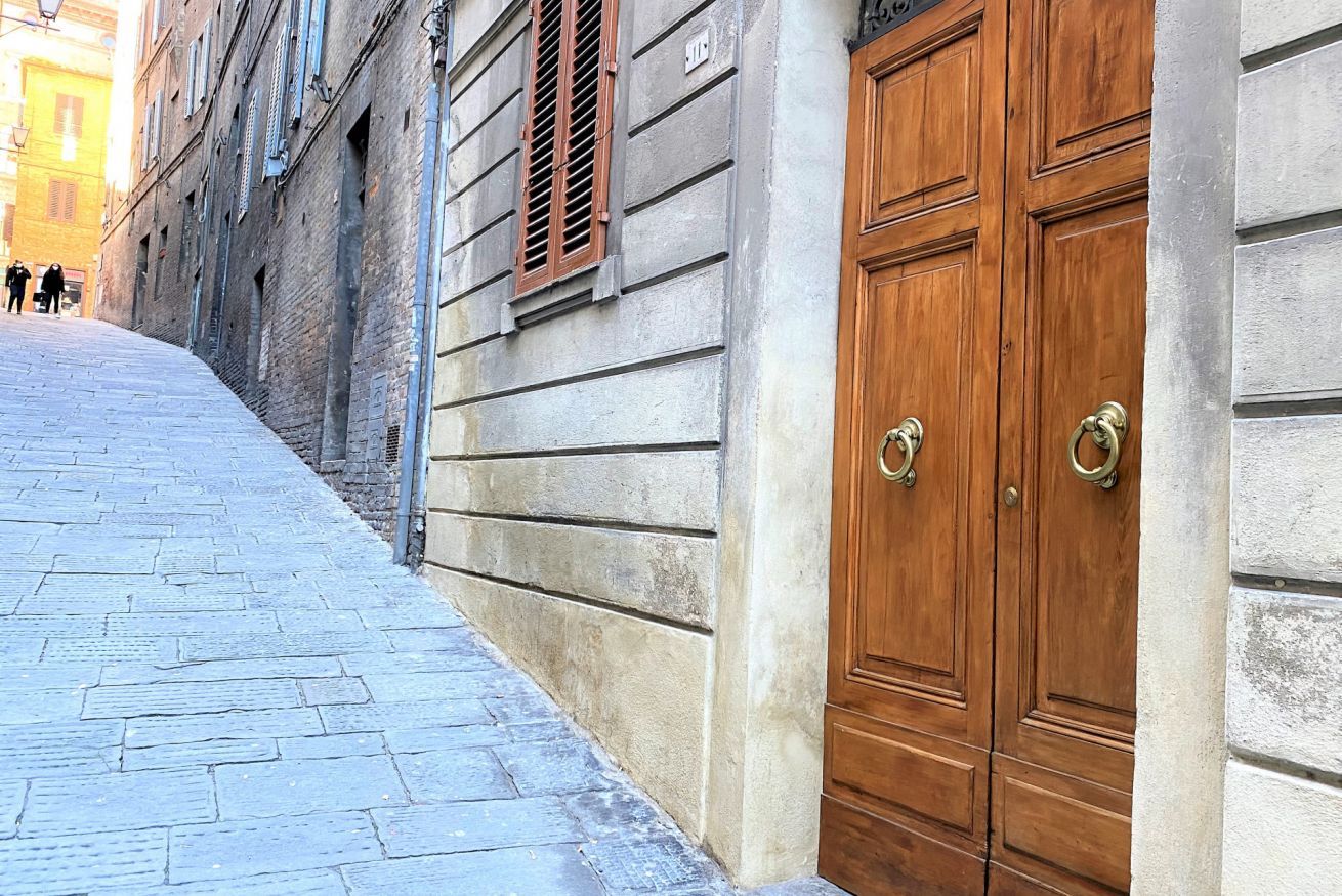 Une ruelle étroite pavée, bordée d’un bâtiment doté d’une porte double en bois et d’une fenêtre avec des volets.