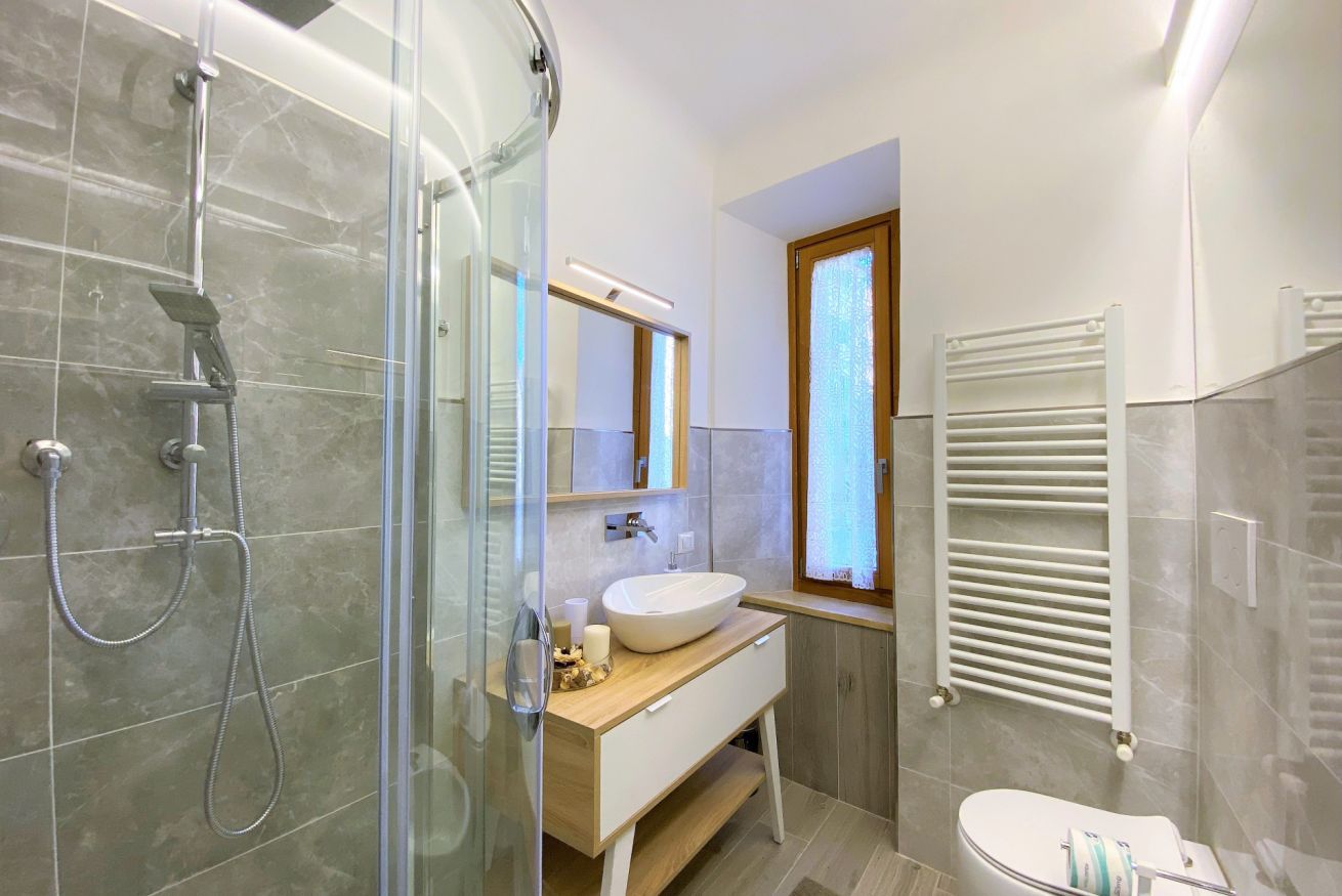 A modern bathroom with a glass-enclosed shower, a wooden vanity with a white sink, and a white toilet.