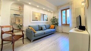 Una sala de estar moderna con un sofá gris, una silla de madera y un televisor de pantalla plana sobre una mesa blanca.