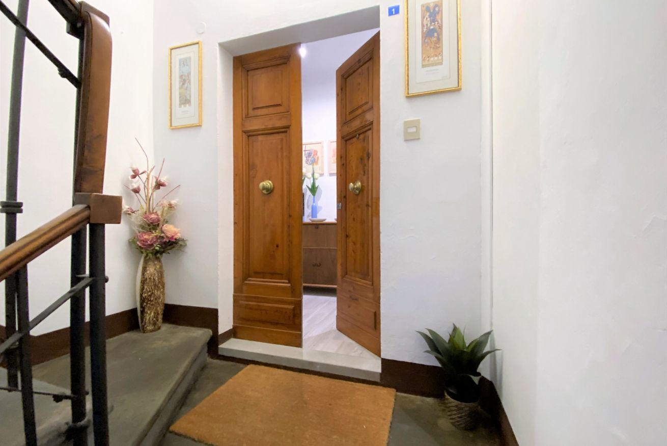 A hallway with wooden doors, a staircase, and a vase with flowers.