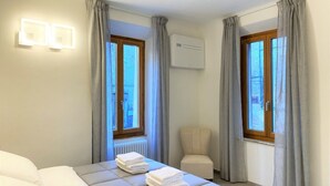 Una habitación de hotel con una cama, dos ventanas con cortinas, un aire acondicionado y una silla.