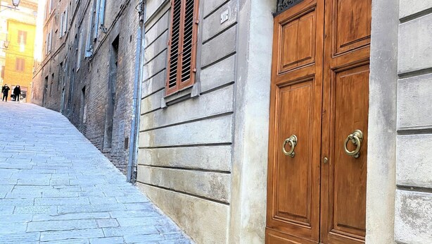 Una estrecha calle adoquinada con un edificio que tiene puertas de madera dobles y una ventana con contraventanas.