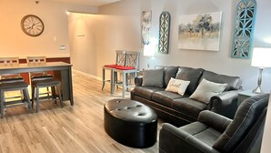 Un salon moderne avec un canapé en cuir, un pouf et un coin repas comprenant une table et des chaises en bois.