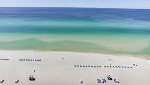 A beach with rows of blue lounge chairs and a few umbrellas, a sandy beach, and a calm sea. - 2 Bedroom in Ocean Villa Resort - Stunning views and all the comforts of home! (Panama City Beach)