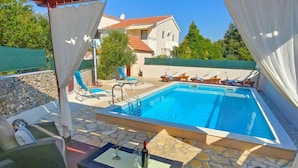 Ein Swimmingpool mit Liegestühlen und einem Tisch, umgeben von Steinplatten und einer Pergola.