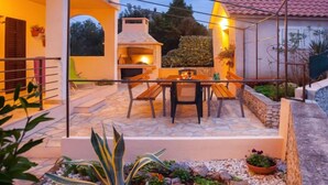 Eine Terrasse im Freien mit Steinboden, einem Tisch mit Stühlen und einem Grill.