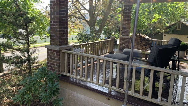 Eine überdachte Terrasse mit einer Ziegelstütze, Holzgeländer und Gartenmöbeln.