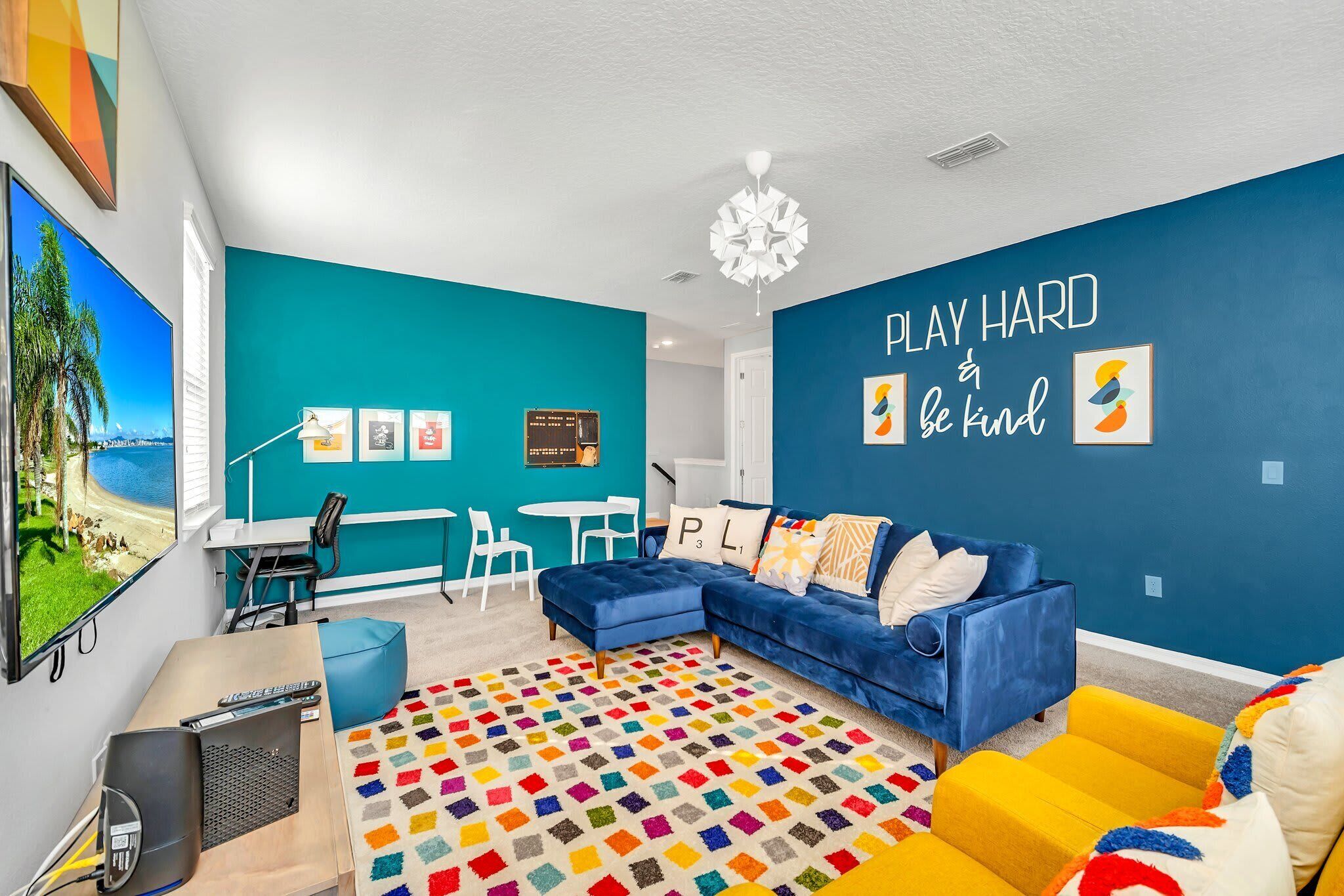 Una sala de estar moderna con una pared de acento color aguamarina, un sofá seccional azul, un tapete geométrico colorido y una frase motivacional en la pared.