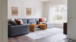 Una sala de estar moderna con un sofá seccional gris, una mesa de centro de madera y dos piezas de arte tejidas colgadas en la pared.