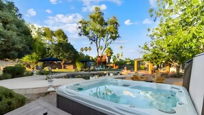 Un jacuzzi en un patio trasero con una pérgola, mobiliario exterior y un aro de baloncesto.