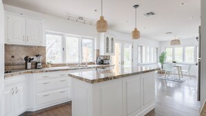 Una cocina amplia con armarios blancos, una isla grande e iluminación colgante.