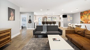 A modern living room with a grey sofa, a brown sofa, a white coffee table, and a wooden cabinet. There is a dining area with white chairs and a table in the background. - Biltmore Highlands by Porter | Luxury Home w/Private Pool and Mountain Views (Phoenix)