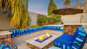 An outdoor seating area with a fire feature, a table, and a large umbrella. - Biltmore Highlands by Porter | Luxury Home w/Private Pool and Mountain Views (Phoenix)