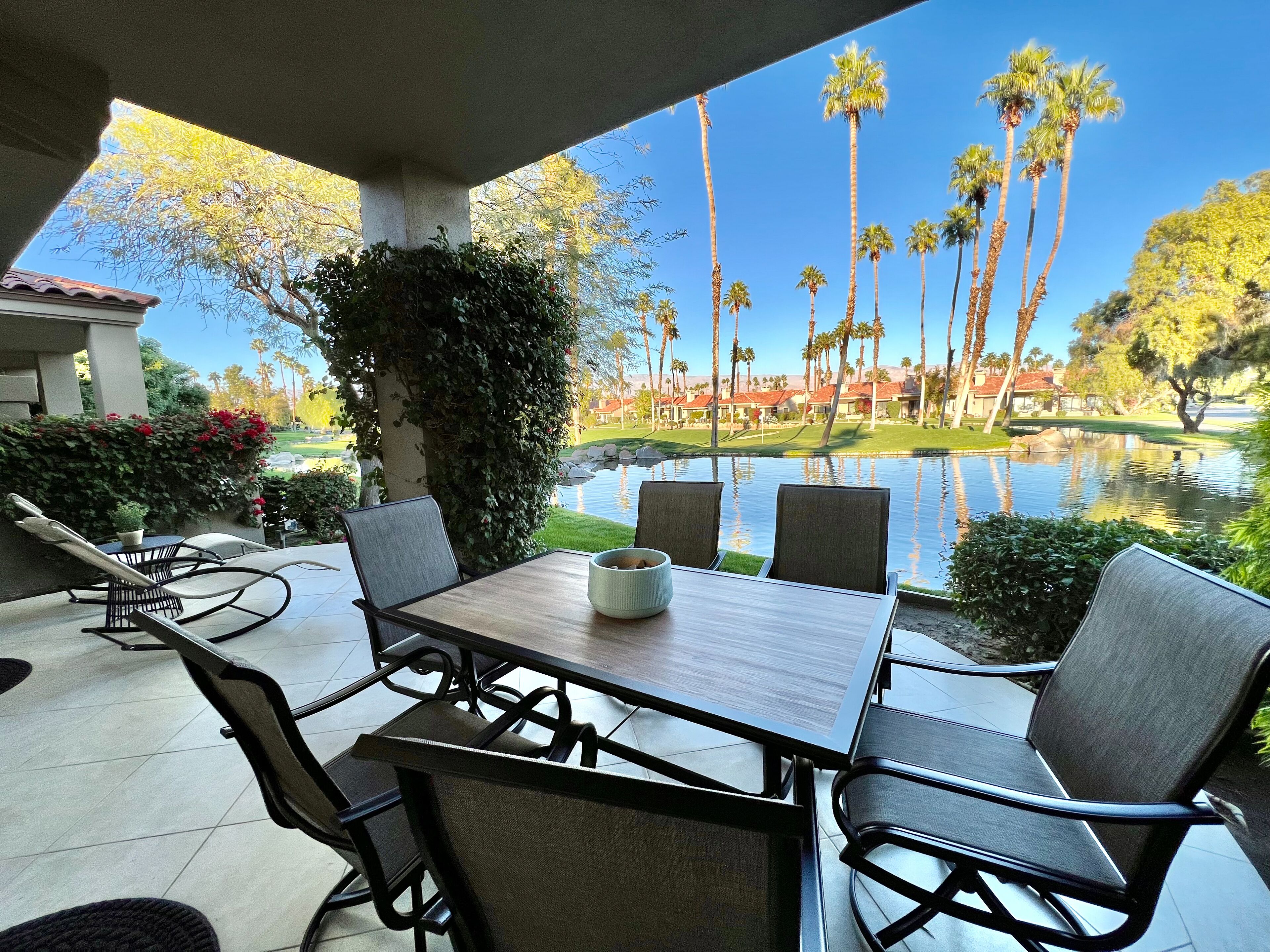 A patio with a table and chairs, overlooking a pond and palm trees.