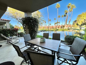 A patio with a table and chairs, overlooking a pond and palm trees.