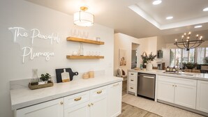 A modern kitchen with white cabinetry, a marble countertop, and a neon sign on the wall.