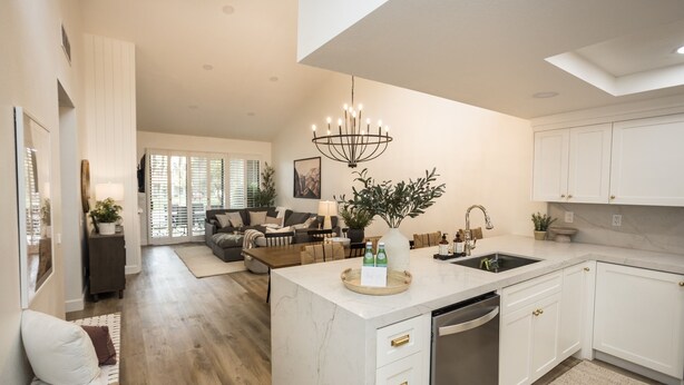 A modern kitchen with white cabinetry, a marble island, and a chandelier.