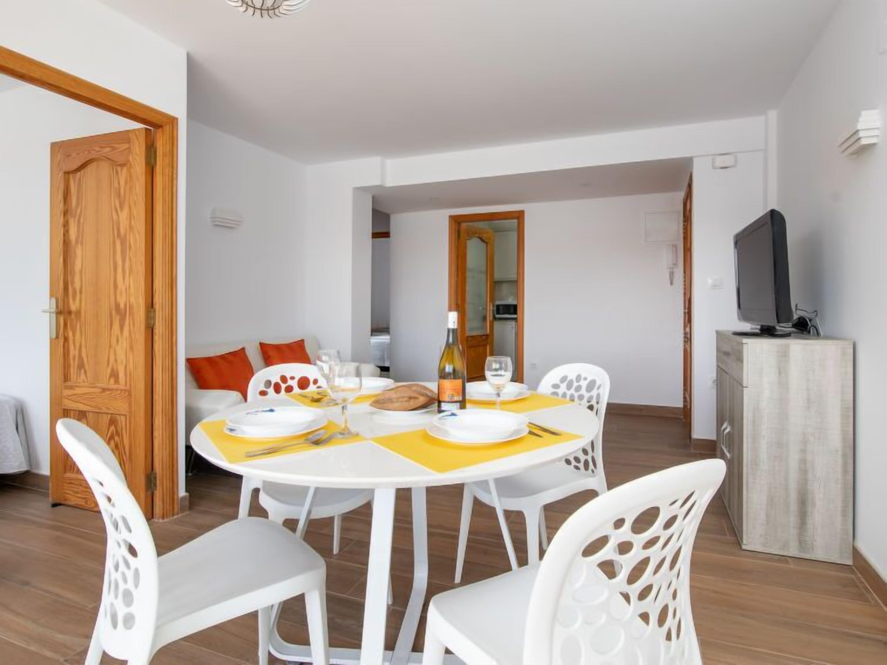 Un coin repas avec une table ronde, des chaises blanches et un téléviseur posé sur un meuble.