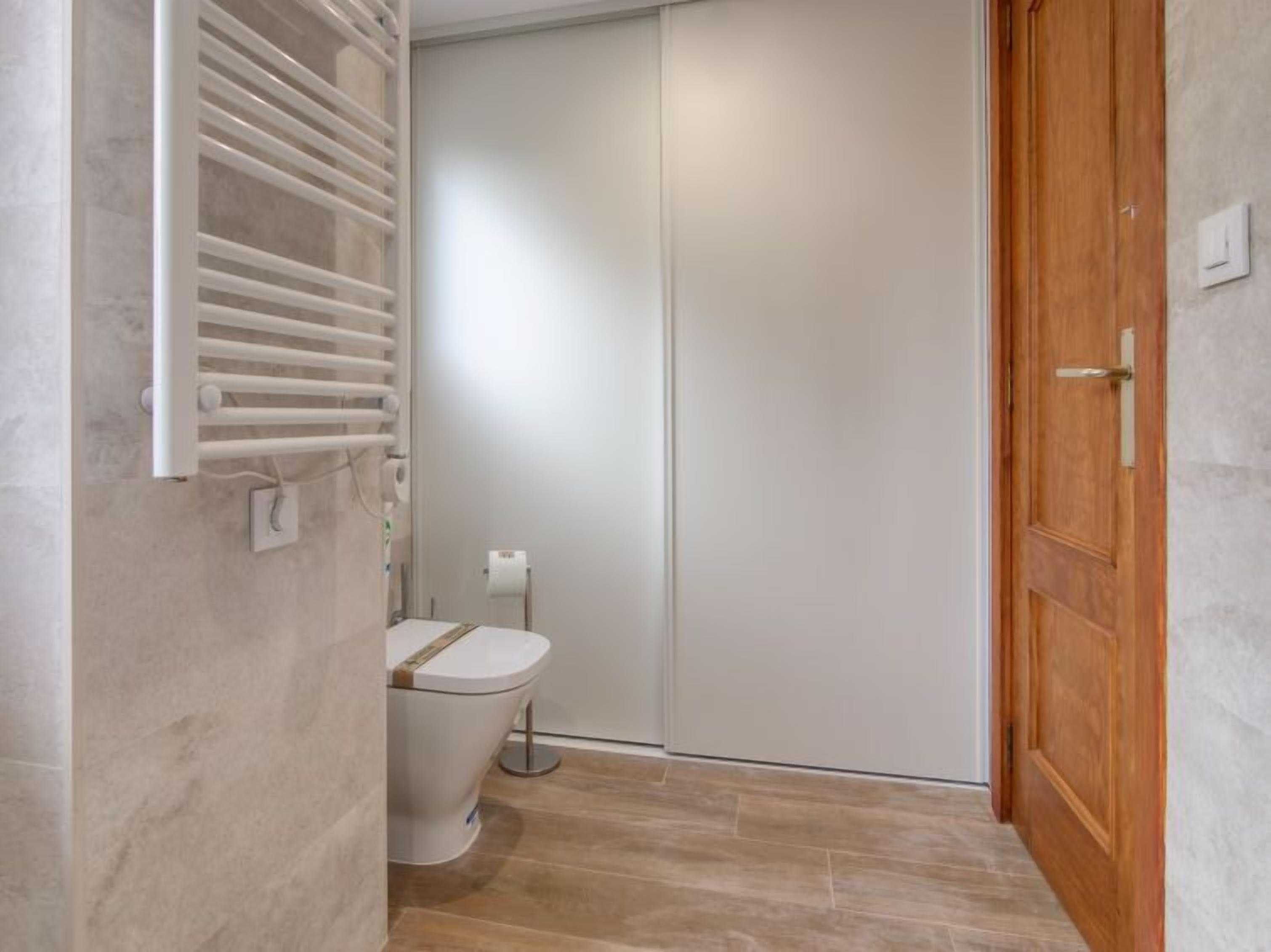 A small, narrow bathroom with a toilet, a towel rack, and a wooden door.