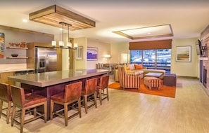 A modern kitchen with a central island, bar stools, and a dining table.
