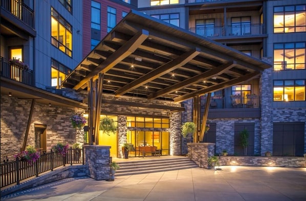 A hotel entrance with a covered patio, stone facade, and multiple balconies.