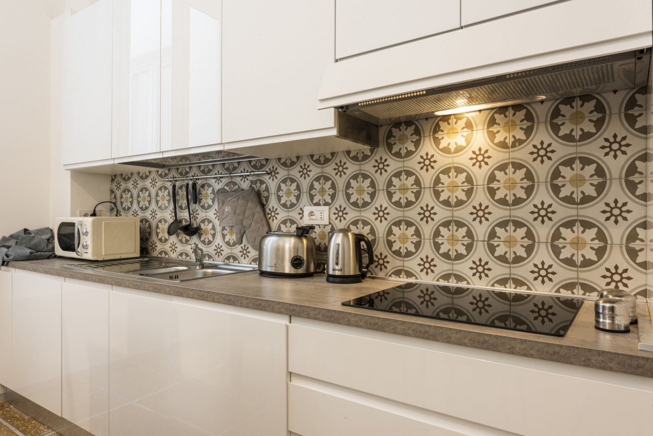 A modern kitchen with white cabinets, a patterned backsplash, a toaster, a kettle, and a sink.