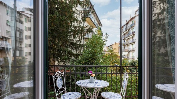 Un balcón con dos mesas redondas y sillas, una planta en maceta y vistas a edificios y árboles.