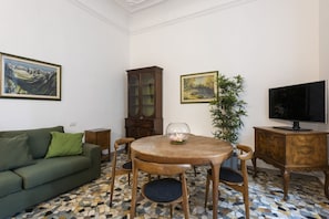 Un salon avec un canapé vert, une table ronde en bois entourée de chaises, un meuble et un téléviseur.
