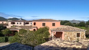 A row of Mediterranean-style buildings with terracotta roofs, stone walls, and arched doorways, surrounded by greenery and hills. - La Ginestra Three-room apartment sleeps 6 (San Teodoro)