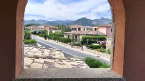 A view through an archway of a residential street with houses, a road, and mountains in the background. - La Ginestra Three-room apartment sleeps 6 (San Teodoro)