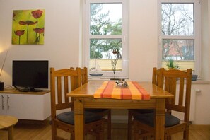 A dining area with a wooden table, four chairs, a television on a cabinet, and a painting on the wall.