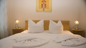 A neatly made bed with white linens and pillows, two bedside lamps, and a painting on the wall. - Dünenresidenz - Apartment directly on the beach, balcony with sea view - Dünenresidenz FeWo (Breege)