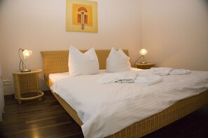 A neatly made bed with white linens and pillows, two bedside lamps, and a single artwork on the wall.