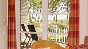 A room with a large sliding glass door leading to an outdoor deck. The deck has a white railing and two black chairs. - Dünenresidenz - Apartment directly on the beach, balcony with sea view - Dünenresidenz FeWo (Breege)