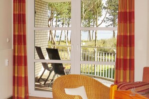 A room with a large sliding glass door leading to an outdoor deck. The deck has a white railing and two black chairs. - Dünenresidenz - Apartment directly on the beach, balcony with sea view - Dünenresidenz FeWo (Breege)