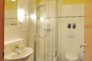 A bathroom with a glass-enclosed shower, a white sink with a soap dispenser, and a toilet.