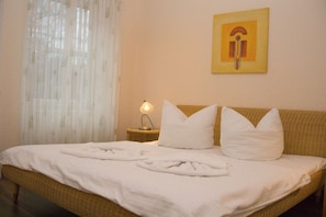 A neatly made bed with white linens and pillows, a bedside lamp, and a framed picture on the wall.