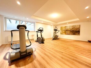 A spacious room with a large window, a treadmill, an elliptical, and a stationary bike. - Dünenresidenz - Apartment directly on the beach, balcony with sea view - Dünenresidenz FeWo (Breege)