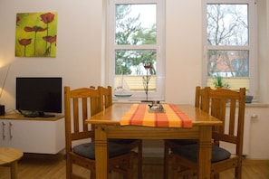 Un coin repas avec une table en bois, quatre chaises, un téléviseur posé sur un meuble et un tableau accroché au mur.
