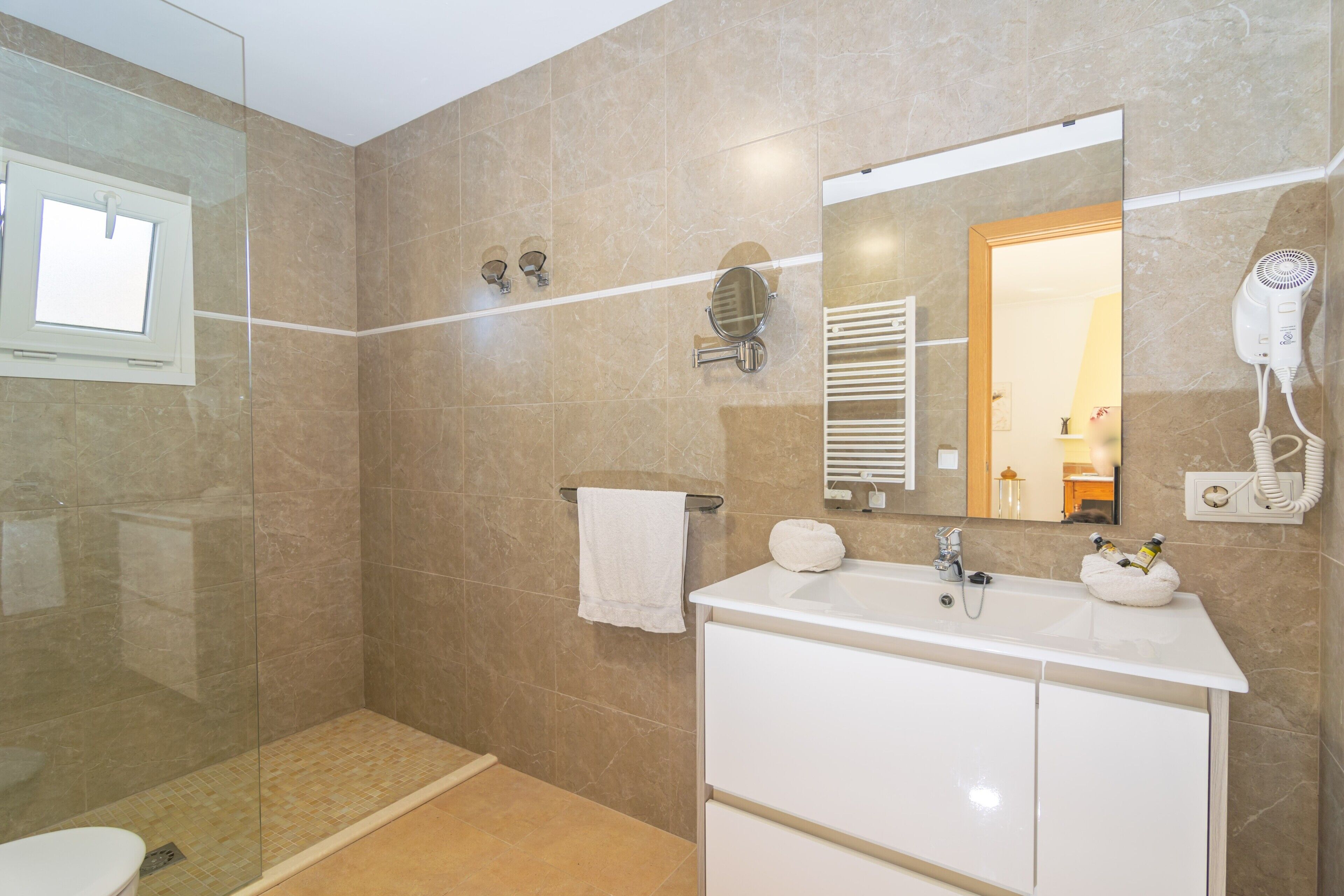 Un baño moderno con cabina de ducha de vidrio, un lavabo blanco con dos cubetas, un espejo y un secador de pelo montado en la pared.